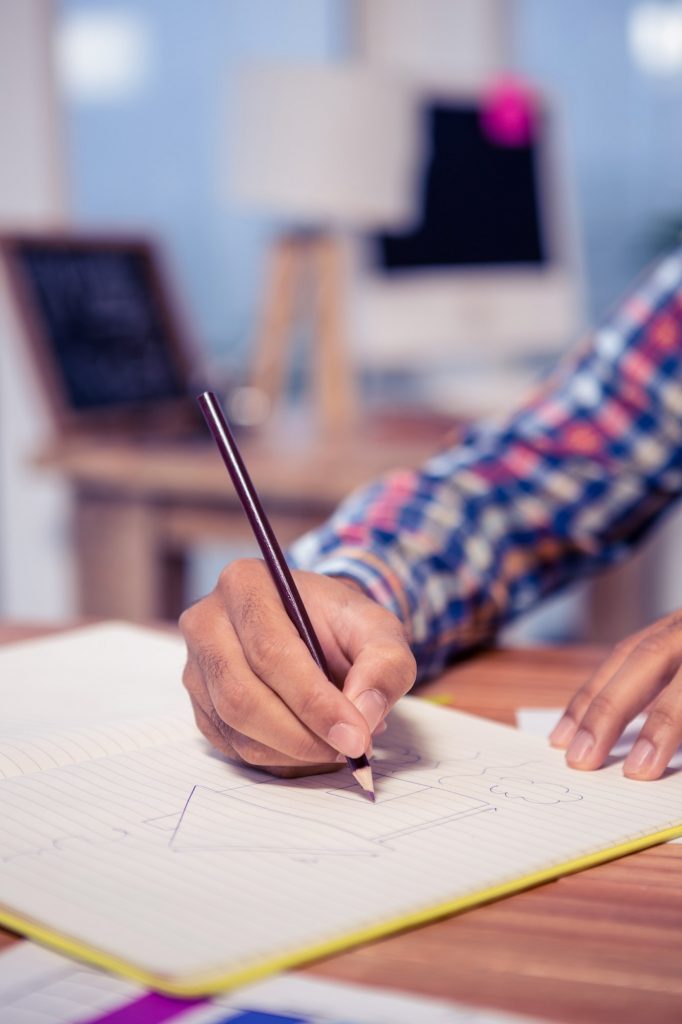 Cropped hand of businessman drawing house in book at desk in office